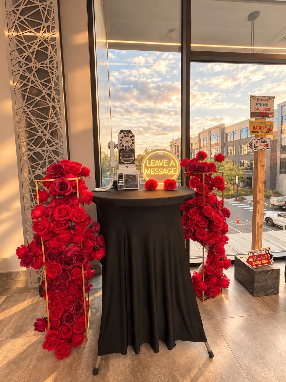 Retro phone guest book under a glowing 'Leave a message' sign, flanked by red rose stands by a window