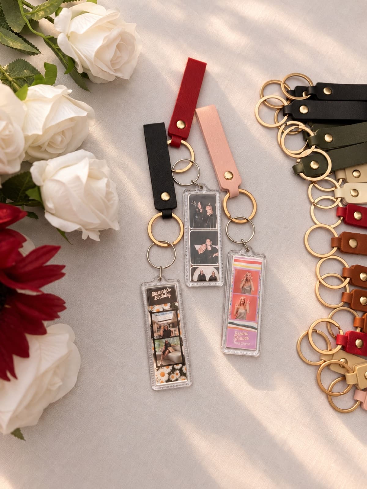 Photo-strip keychains with leather straps in a range of colors, arranged with white roses