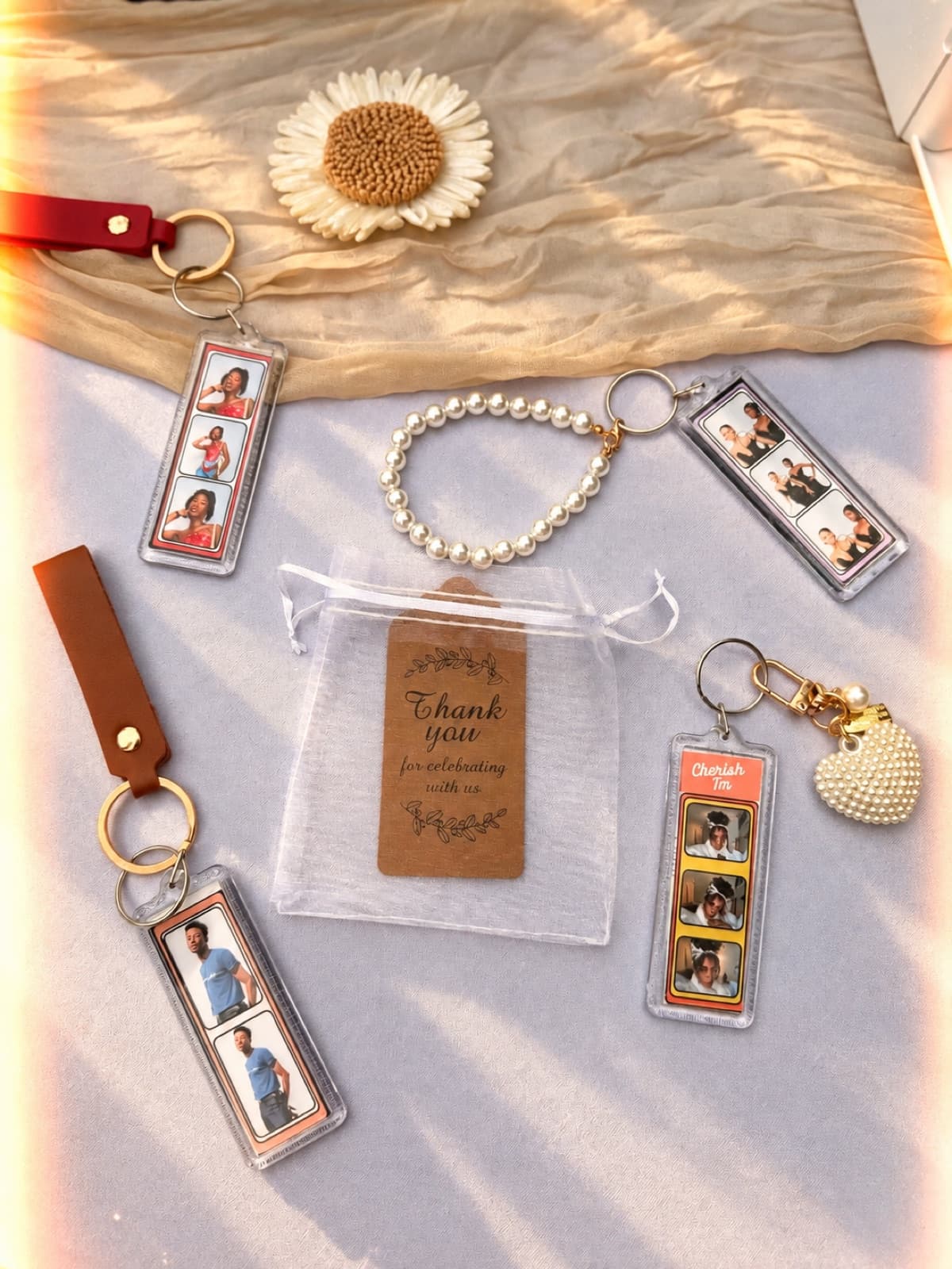 Finished photo-strip keychains with leather and pearl straps beside a 'Thank you for celebrating with us' favor bag