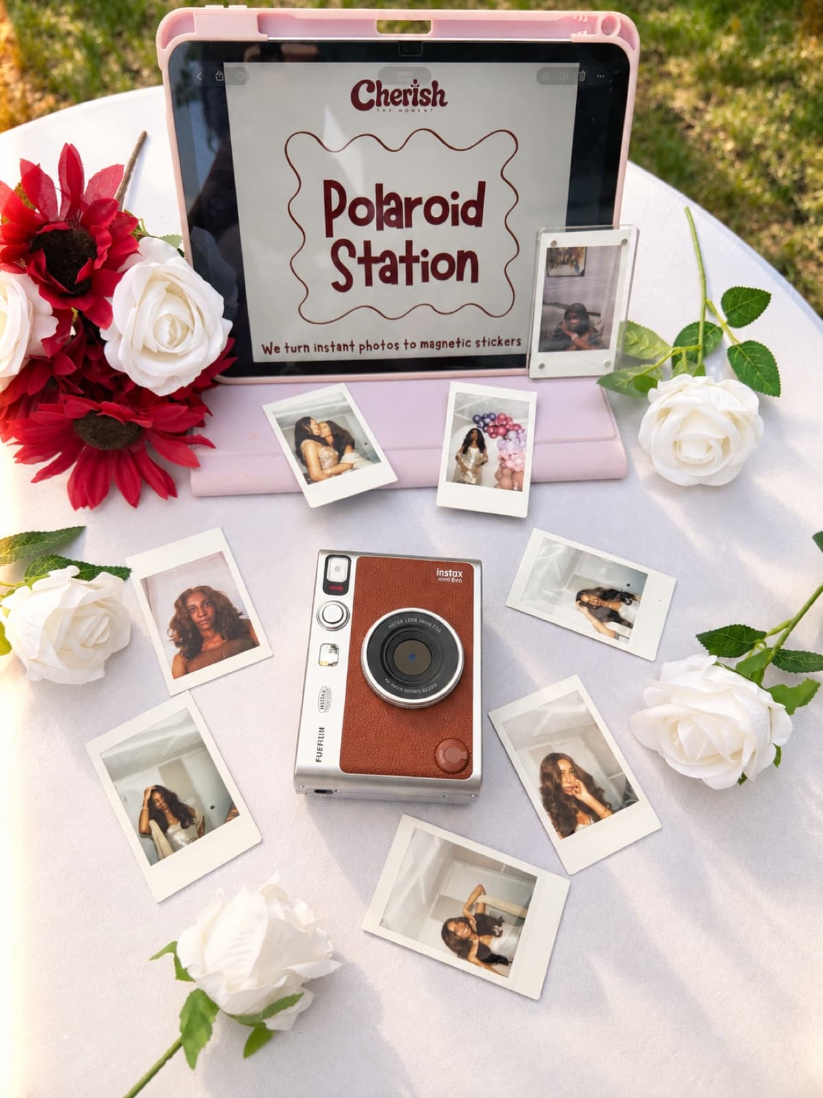 Polaroid Station on a pink tablet stand surrounded by white roses and guest photos