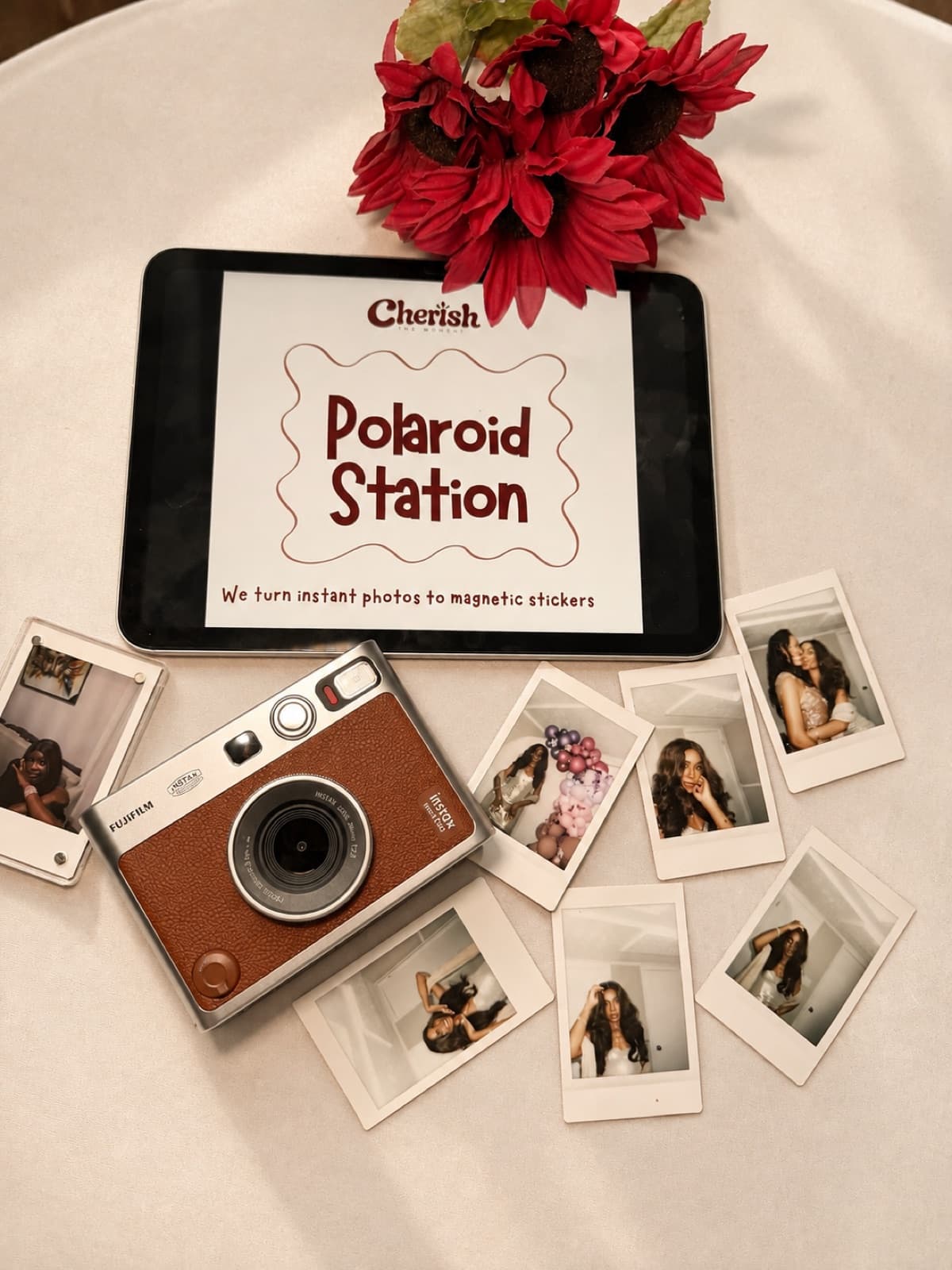 Instant prints of guests spread around a brown Instax camera and the Polaroid Station sign